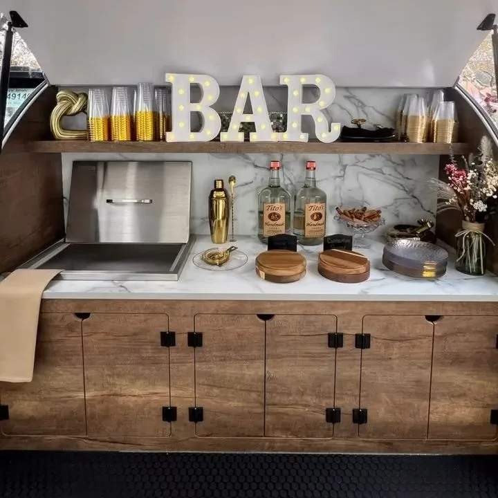 The back bar inside the trailer: an ice well, bar tools, garnishes and light-up BAR letters above wood cabinets