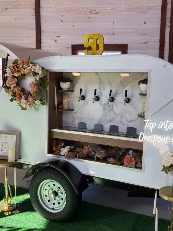 The trailer with a floral wreath and a gold 50 on top, set up on turf inside a wood-paneled room