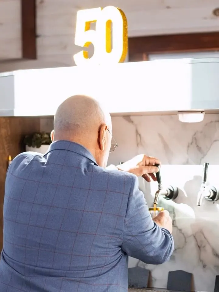 A guest in a blazer pours his own drink from a tap at a 50th birthday