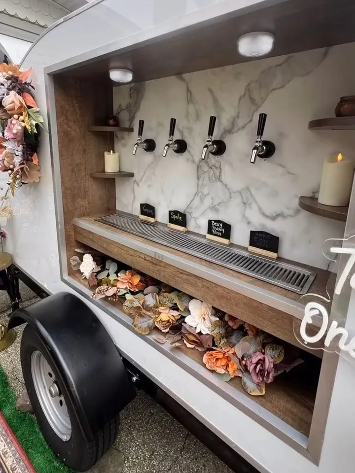 The side window of the trailer: four taps over a marble wall, with a shelf of dried flowers below