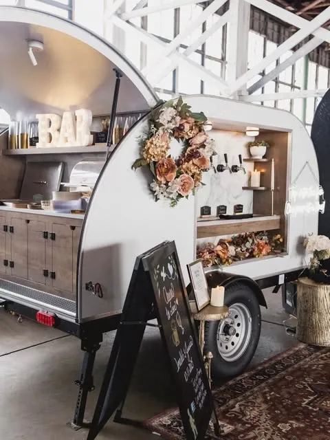 The trailer decorated with a dried-flower wreath and BAR marquee letters inside an event venue